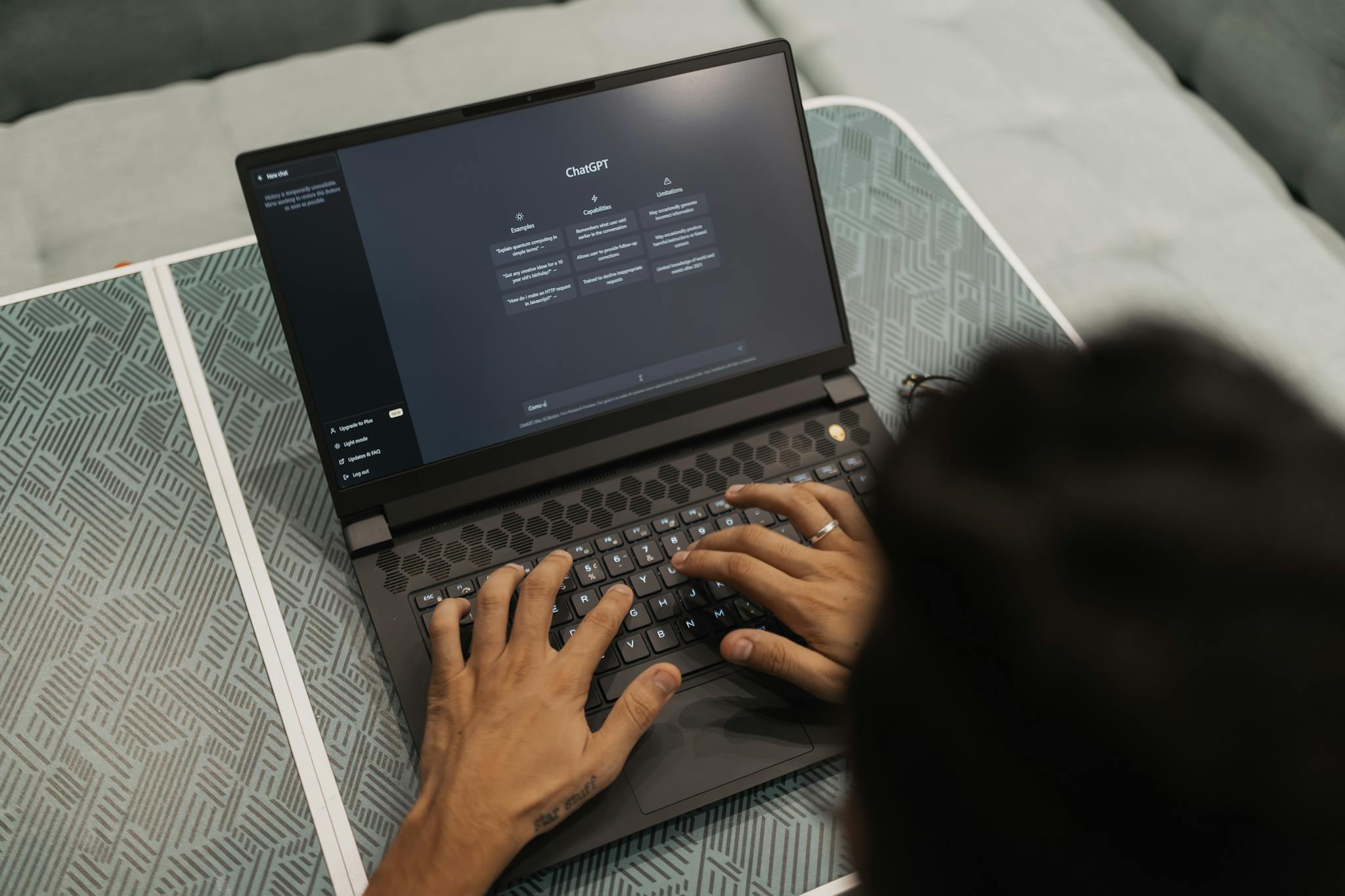 Home Close-up of hands typing on a laptop displaying ChatGPT interface indoors.